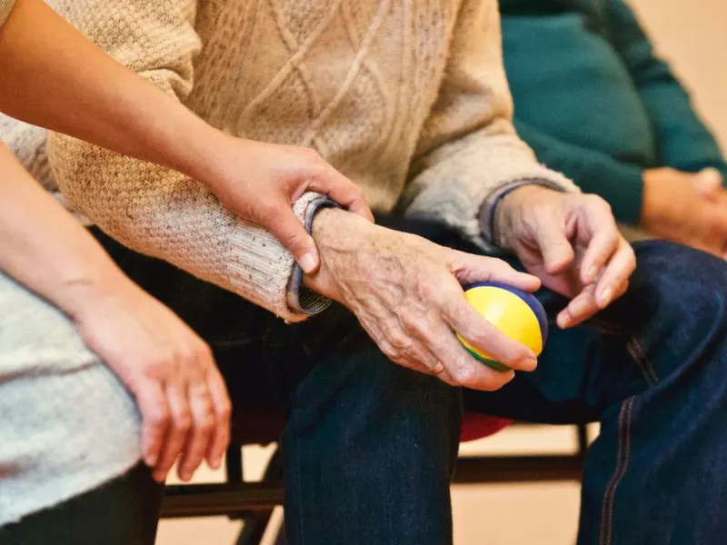 A caregiver guides a senior client through a hand exercise at home