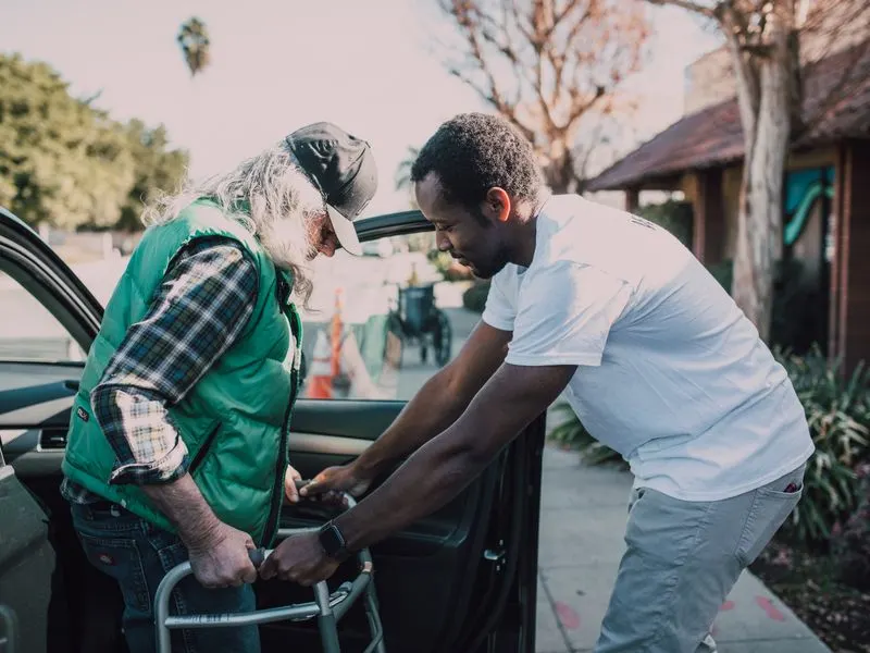 A physical therapist helps a senior man practice walking with his walker at home
